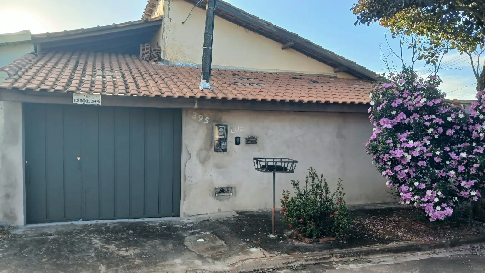 Fachada antes do serviço: parede bege com massa descascando e portão de garagem cinza escuro desbotado.
