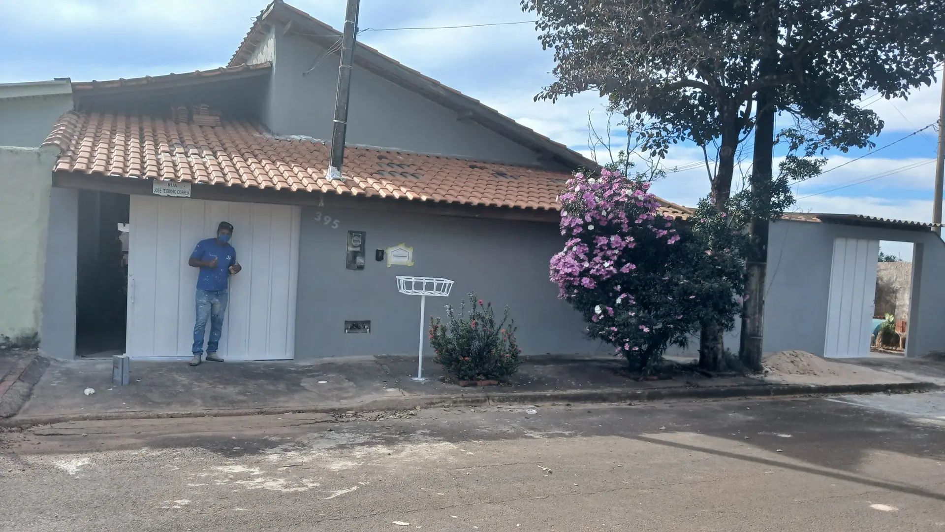 Anderson em frente a uma fachada recém-pintada em cinza, com portão de garagem branco.