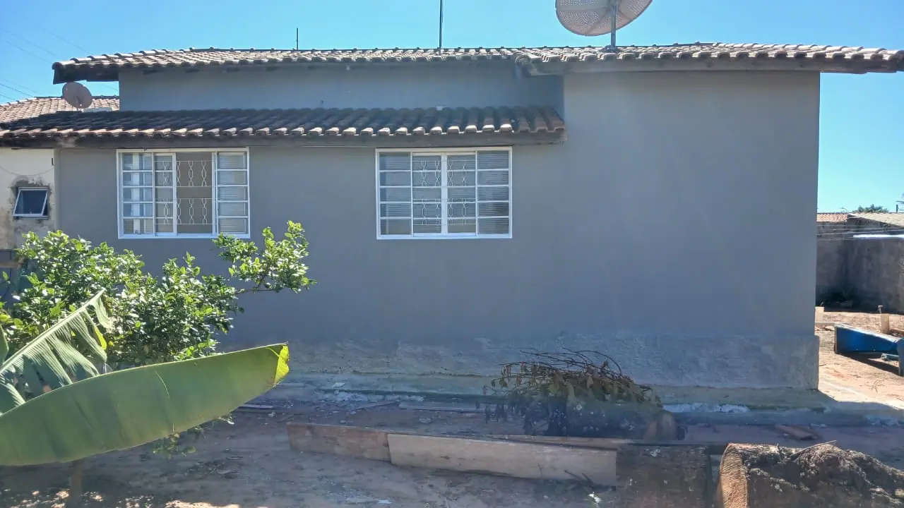 Lateral de casa pintada em cinza claro com faixa de rodapé e esquadrias brancas.