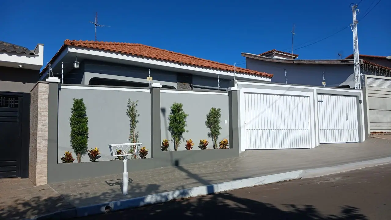 Fachada com muro cinza, nichos de plantas e dois portões brancos pintados por Anderson Pintor.